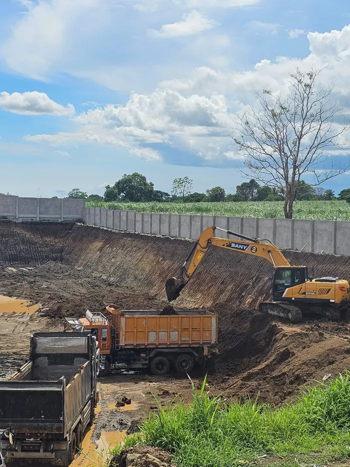 Excavator loading dump trucks during earthworks along a new perimeter fence